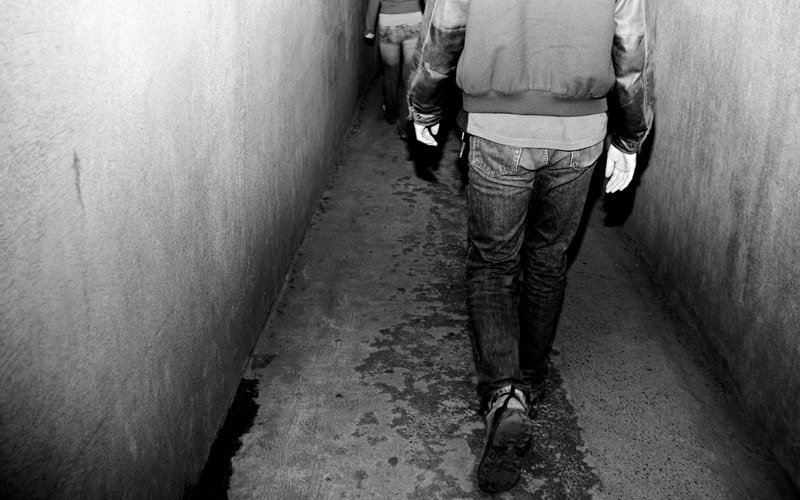 写真：コンクリートに覆われた細い廊下を歩く後ろ姿を撮影したモノクロ写真